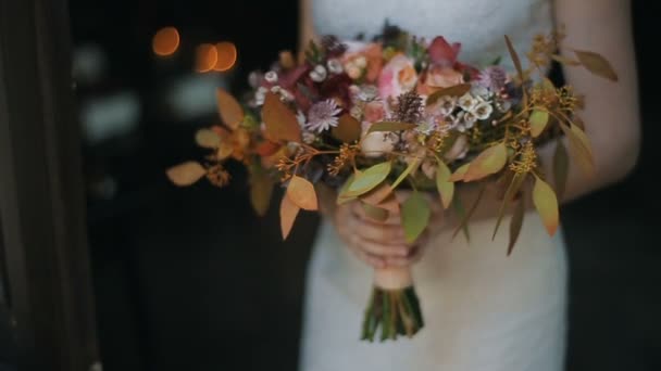 Bröllop bukett i bruden händer inomhus. Brinnande ljus på en bakgrund. Bruden håller vackra bröllop bukett av olika blommor. — Stockvideo