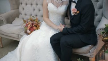 Kapalı bir kanepede oturan tutan eller, mutlu damat ve gelin düğün çifti. Aşk gelin ve damat, düğün günü Genç Çift.
