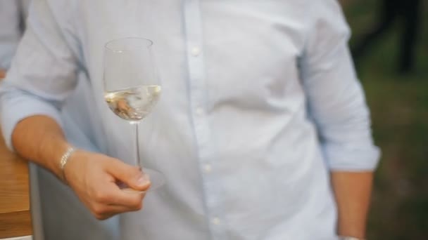 Gli uomini scuotono il vino bianco in un bicchiere da vino trasparente. Un uomo che assaggia un bicchiere di vino bianco . — Video Stock