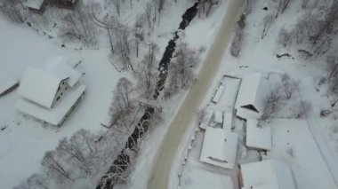 Karpatya dağlarındaki bir köyün üzerinden ve yanındaki kayak merkezinin üzerinden uçacağız. Nehir boyunca uzanan hava yolu ve dağ köyünde kar altında evler. Kışın kırsal alan. Carpathian kayak merkezi.