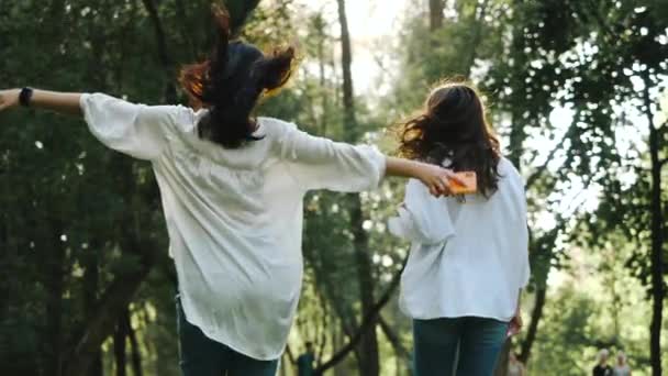 Dos chicas morenas jóvenes felices riendo y bailando en cámara lenta, vista rara. Feliz impresionante Las mujeres con el pelo soplando en el viento mirando a la cámara, saltando y sonriendo . — Vídeos de Stock