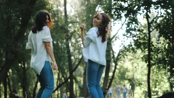 Dos chicas morenas jóvenes felices riendo y bailando en cámara lenta. Feliz impresionante Las mujeres con el pelo soplando en el viento mirando a la cámara, saltando y sonriendo . — Vídeo de stock