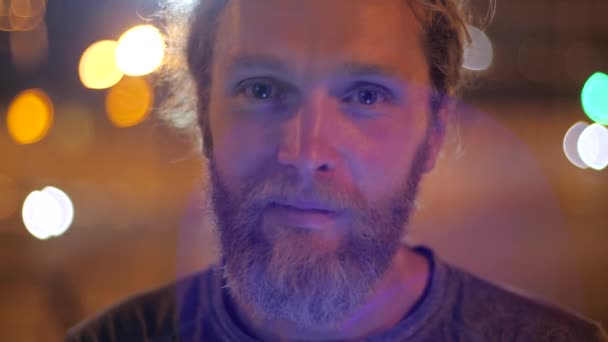 Portrét pohledného dlouhosrstého vousatého mladíka, který vypadá ohromeně zamyšleně, přemýšlí o čekání na dojíždění, pozoruje něco na pozadí pohybujících se večerních světel. — Stock video