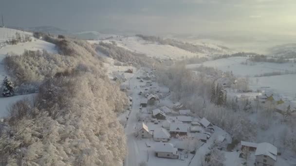 Luchtpanorama van een bergdorp in de winter bij zonsopgang. Huizen onder sneeuw in bergdorp. Landelijk landschap in de winter. Vlucht over een dorp in de Karpaten en een skigebied ernaast. — Stockvideo