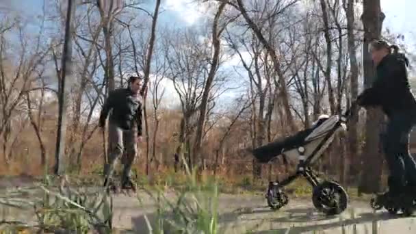 Rollerfamilie spaziert im Herbst mit Baby in einem gemütlichen Stadtpark. Papa tanzt und unterhält das Baby. heller, sonniger Tag, Zeitlupe. Sporterziehung und gesunde Leidenschaft. — Stockvideo