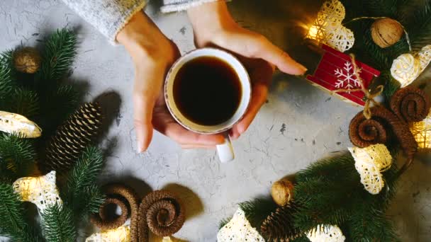 A karácsony családi ünnep. A gyönyörű női kezek egy csésze fekete teát vagy kávét tesznek az asztalra, a férfi kezek pedig összekulcsolják a nőkét. Az asztalon vannak karácsonyi dekorációk, egy koszorú lucfenyő ágai. — Stock videók