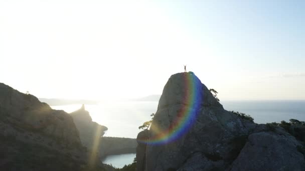 Silhouette aerea di una ragazza in piedi sulla cima di una montagna sul mare all'alba. Volo sopra Giovane donna attiva sulla cima in Crimea con le braccia tese. Alpinista donna — Video Stock