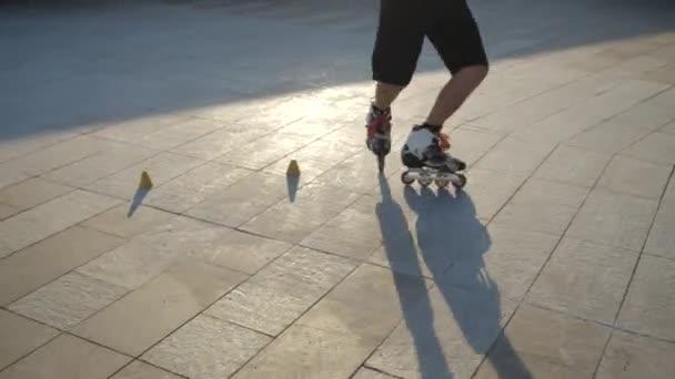 Close-up benen van een jonge man professioneel schaatsen tussen kegels op een mooie avond zonsondergang in een stadspark. Freestyle slalom Rolschaatsen tussen kegels. — Stockvideo