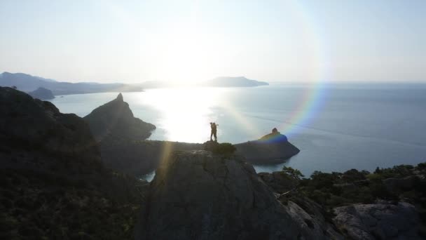 Flygsilhuett av ett ungt kärleksfullt par som står på toppen av ett berg över havet vid soluppgången och kysser. Flyg över Unga aktiva bergsklättrare man och kvinna på toppmötet i Krim — Stockvideo