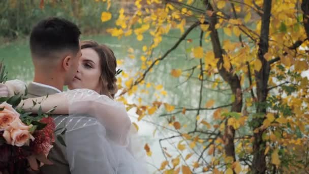 Gros plan portrait de Mariée et marié embrassant près d'un lac dans la forêt d'automne parmi les arbres d'automne colorés. Jeune attrayant heureux aimer les jeunes mariés dans un parc au ralenti . — Video