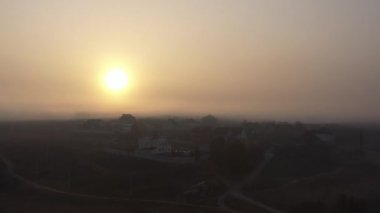 Parlak güneş bir sonbahar sabahı küçük bir kasabanın üzerinde parlar. Sabah sisli gökyüzü. Hafif yağmur ve rüzgâr esiyor. Evlerin üzerinde güzel bir gün doğumu. Üst ve yan görünüm yavaş çekimde.