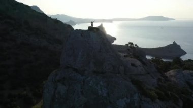 Gün doğumunda denizin üzerinde bir dağın tepesinde duran bir kızın etrafında dinamik uçuş. Kırım 'daki zirvede kollarını açmış genç aktif bir kadının üzerinden uçuyor. Bayan dağcı silueti