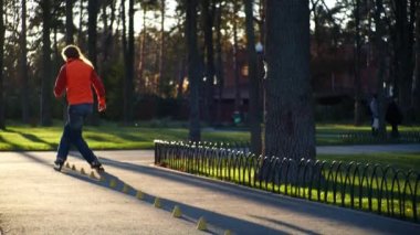Profesyonel bir erkek patenci bacaklarını kavuşturup külahların arasına girer ve iki arka tekerleğin üzerinde durur. Bir adam ağır çekimde paten kayar..