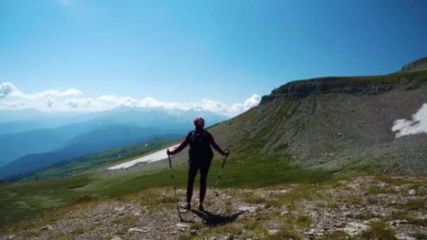 Η Λαίδη ανεβαίνει στα όμορφα βουνά του Καυκάσου. Νεαρή γυναίκα με σακίδιο και κοντάρια πεζοπορίας στο δρόμο για την κορυφή του βουνού κάνει μια παύση για να παρατηρήσει φανταστική θέα από ύψος. — Αρχείο Βίντεο