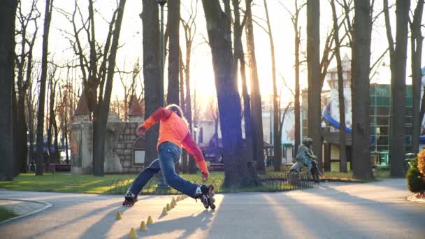 Entrenamiento de un rodillo profesional que patina hábilmente en el parque central de la ciudad y realiza giros complejos entre conos de entrenamiento. Estilo de vida activo y saludable. Vista lateral en cámara lenta . — Vídeos de Stock