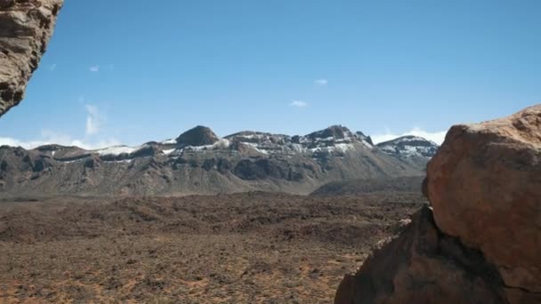 Krásná horská scenérie na Tenerife, Kanárské ostrovy. Pohled na skalnatou sopečnou poušť a obrovský kráter sopky Teide. Modrá obloha a mraky na obzoru. Zpomalený pohyb fotoaparátu mezi kameny. — Stock video