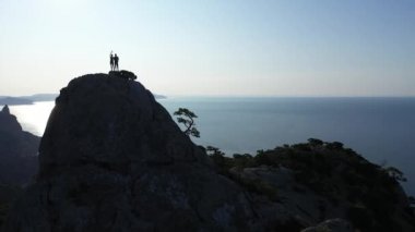 Gün doğumunda denizin üzerinde bir dağın tepesinde el sallayan genç bir çiftin hava silueti. Genç aktif dağcıların üzerinden uçmak Kırım 'daki zirvede erkek ve kadın