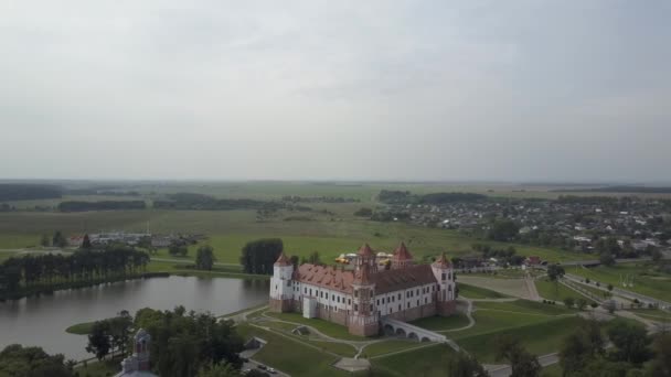 Körkörös légi fotózás a Mir-kastély négykopteréből Fehéroroszországban, amely Mir városában található, fákkal körülvéve, és egy kis tó közelében található. Top nézet lassított felvételben. — Stock videók