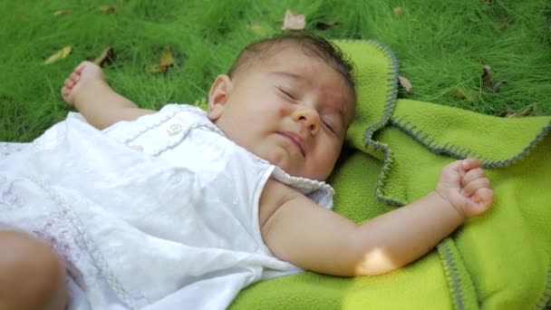 Cute infant baby sneezes two time loudly in slow motion, close-up view. Dreamy newborn baby infant lying on a grass outdoors.Infant baby child. Little girl lies on a rug on grass in a park. — Stock Video