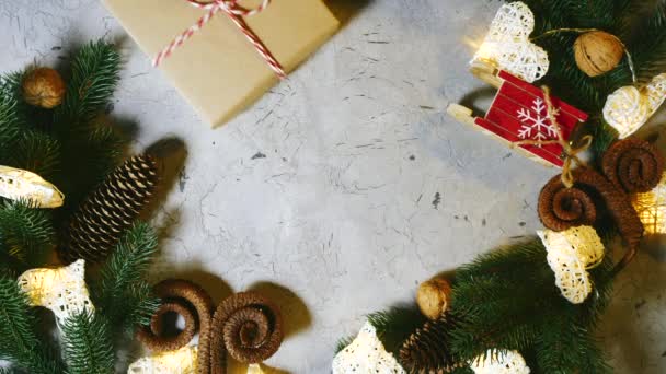 Dobrá zimní nálada čeká na Vánoce. Lidské ruce dali vánoční dárek na zbytek dekorací a hraček. Nový rok se blíží. Na stole leží věnce, kornouty, ořechy. Pohled shora. — Stock video