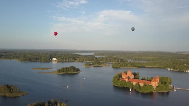 El famoso castillo de Trakai en una isla en medio del lago Galve, rodeado de árboles. Disparando al cielo desde una altura en la que un par de globos grandes son visibles. Monumento en Lituania, Vilnius . — Vídeos de Stock