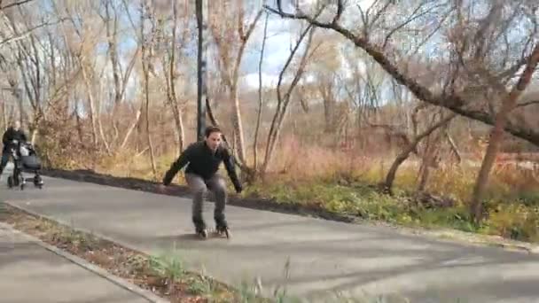 Deporte padres jóvenes con un niño caminar en el parque soleado otoño en patines. Papá se adelanta y hace un truco de saltos. Movimiento lento . — Vídeo de stock