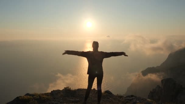 Silhuette Young Mujer brazos extendidos observando una hermosa puesta de sol dramática sobre un mar de una alta montaña en Crimea . — Vídeo de stock