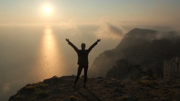 Ung kvinna Silhuette med armarna upp och ut observera en vacker dramatisk solnedgång ovanför ett hav från ett högt berg i Krim. — Stockvideo