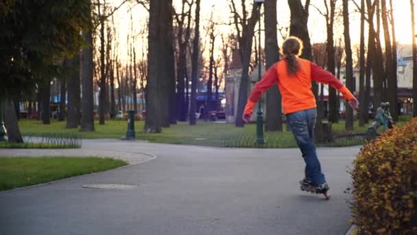 Il giovane pattinatore a rotelle dai capelli lunghi sta ballando tra i coni in una bella serata in un parco cittadino. Slalom stile libero Pattinaggio a rotelle tra coni al rallentatore . — Video Stock