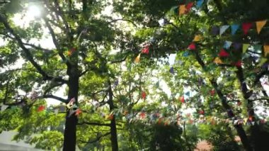 Bayram için renkli kağıt bayraklardan oluşan bir çelenk. Çocukların doğum günü partisi için bir sahne. Doğayı ağaçların arka planına karşı süslemek. Bunting flaması - Çarşaflardan renkli bayraklar.