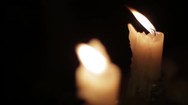 Пара горящих свечей в темной комнате. Две восковые свечи с близкого расстояния горят в темной комнате на фоне ярко мерцающих бликов. Размытый фон мерцающих и горящих свечей. Уютная атмосфера . — стоковое видео