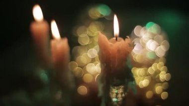 Parlak mumlar, karanlık bir odada, arka planda parlayan parlak ışıklar karşısında yanar. Bir projektörün çok renkli çiçeklerinin arka planında yanan mumlar şeklinde rahat bir atmosfer..