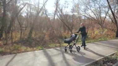 Genç bir aile sonbaharda sabah parkında sepetle gezer. Babam numaralar yapıyor. Yavaş çekim.