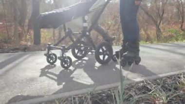 Genç anne ve baba, sonbaharda güneşli bir havada bebekleriyle birlikte paten üzerinde yürüyorlar. Aşağı görünüm Yavaş hareket.
