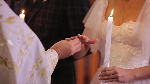 Vista ravvicinata di mani di prete che mettono fedi nuziali alla mano di una sposa. Sposi novelli durante la cerimonia nuziale nella chiesa cristiana . — Video Stock