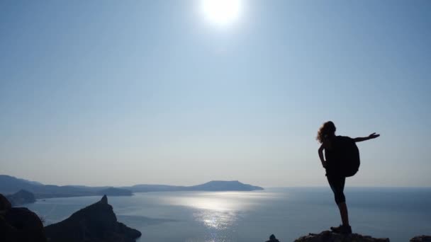 La niña conquistó una roca alta y admira la vista del mar y la sal en el cielo despejado. Mujer atlética levanta las manos y disfruta de la belleza de la naturaleza bajo los rayos del sol en cámara lenta . — Vídeos de Stock