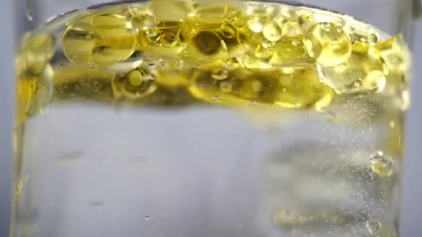 Des ampoules jaunes flottent dans l'eau. L'huile est versée dans un récipient avec de l'eau et des bulles jaunes sont créées. Un verre d'eau est rempli de liquide jaune, vue rapprochée. Bulles d'huile dans l'eau claire . — Video