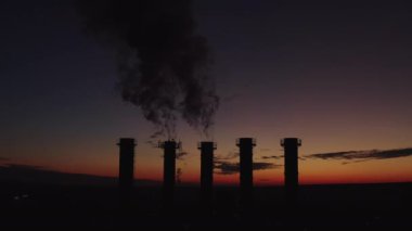 Dumanı tüten bir termik santralin üzerinde güzel bir gün batımı. Güneş soğutma kuleleri ve bacaların üzerinde hareket eder. Kalın duman yükselir. Baca aracılığıyla çevre kirliliği. Beş borudan oluşan siluet.