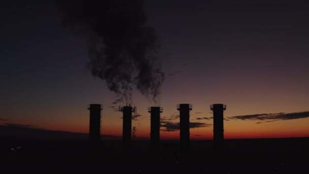 Vacker solnedgång över ett rykande värmekraftverk. Solen rör sig över kyltorn och skorstenar. Den tjocka röken stiger högt. Miljöföroreningar genom skorstenar. Silhuett av fem rör. — Stockvideo