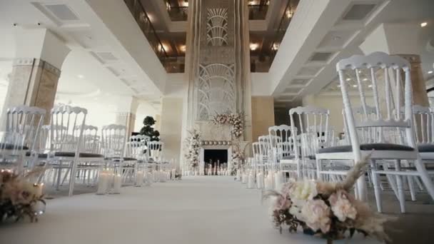 Piękna sala weselna z białymi krzesłami i szklankami ze świecami na podłodze. Atrakcyjne białe wnętrze. Sala wesel i uroczystości. Przytulny i ładny biały pokój z kwiatami i świecami. — Wideo stockowe