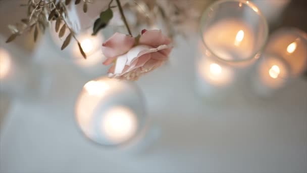 Rose de couleur blanc-rose dans un vase au-dessus des verres avec des bougies, vue de dessus en face de la maison. De belles fleurs pour la mariée sont dans le bureau d'enregistrement. Un cadeau romantique pour une fille en vacances . — Video