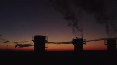 Akşam kentinde günbatımı arka planında kazan dairesi. Kalın duman bacalardan çıkar ve yükselir. Çevre kirliliği. Ülkenin sanayisi. Birkaç soğutma kulesi üst görüntü çekimi.