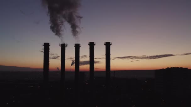 Siluetas de cinco torres de refrigeración contra el telón de fondo de una gran ciudad y puesta de sol. Hermosa puesta de sol sobre una planta de energía térmica humeante. La cámara se mueve sobre torres de refrigeración y chimeneas. Sala de calderas . — Vídeos de Stock