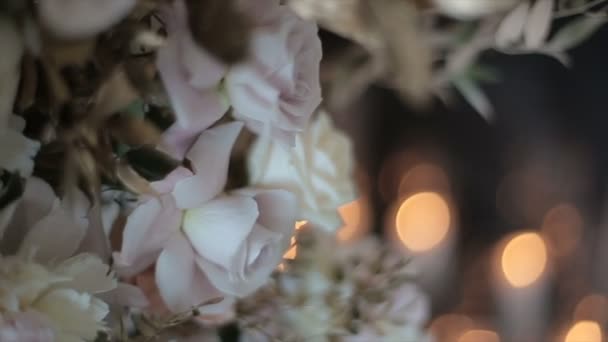 Snow-white roses stand in a vase against a background of blurry flickering glare of light and candles. Beautiful flowers for a wedding in the middle. The flickering of lights conveys a festive mood. — 비디오