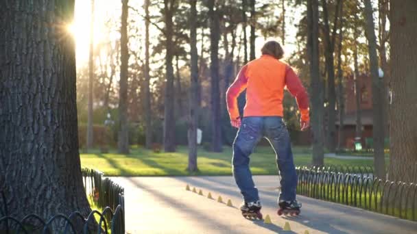 Homme sur roulettes effectue divers tours et promenades entre les cônes d'entraînement, croisant ses jambes. Formation professionnelle de patins à roulettes dans un parc de la ville en automne par temps ensoleillé. Dos tourné au ralenti . — Video