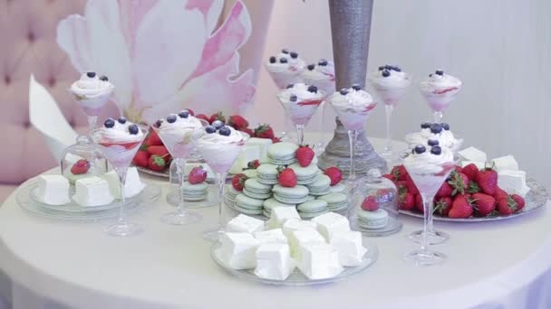 Mesa blanca de boda, cubierta de dulces. Unos deliciosos vasos de helado con crema y bayas, fresas, macarrones y delicias turcas blancas. Dulce mesa para una boda. Diente dulce . — Vídeos de Stock