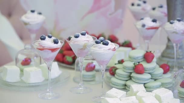 Elegante mesa blanca con dulces para los huéspedes que vinieron de vacaciones. Una fiesta de bodas con deliciosos dulces como helado con crema y bayas, fresas, macarrones y delicias turcas blancas . — Vídeo de stock