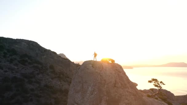 Снимок с воздуха горы Караул-Оба и человека с рюкзаком, который взобрался на вершину. Мужчина поднялся на одну из вершин горы на фоне заката и Черного моря в Крыму — стоковое видео