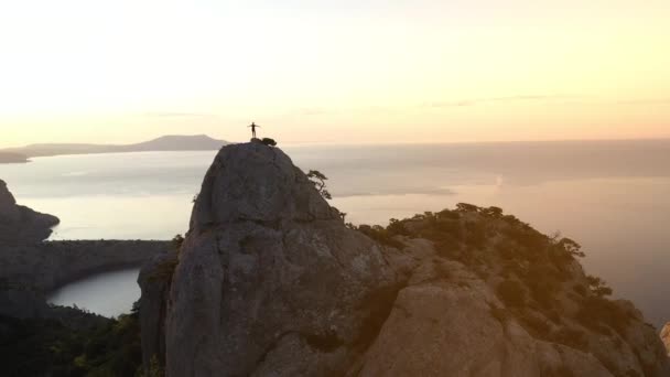 Schießen von oben auf die Person, die den Berg Karaul-oba auf der Krim, Ukraine erobert hat. der berühmte Berg der Halbinsel am Abend vor dem Hintergrund des Sonnenuntergangs und des Schwarzen Meeres. Mann an der Spitze. — Stockvideo