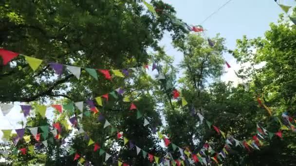 Feestelijke slinger van veelkleurige papieren vlaggen voor de vakantie. Landschap voor een kinderfeestje. Decoratie op de natuur tegen de achtergrond van bomen. Bunting banner - kleurrijke vlaggen van vellen. — Stockvideo